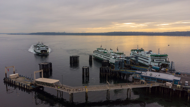 Two ferries docked at Vashon terminal on calm water during a golden sunrise with a third ferry about to dock.