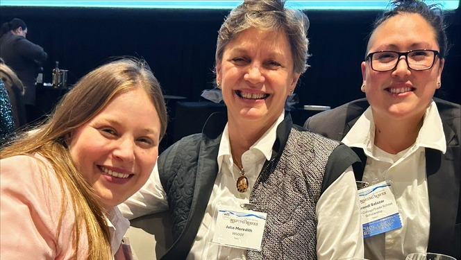 Three people smiling at a table with event name tags in a conference setting.