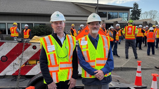 Two people wearing safety gear gathered near a building.