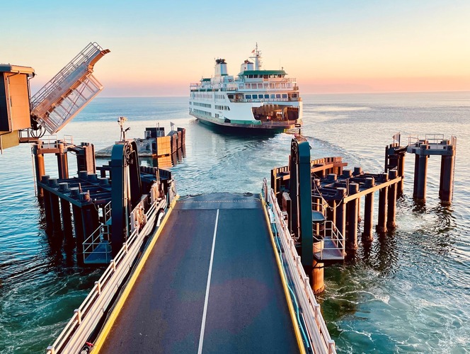 Ferry approaching a dock at sunrise or sunset, with pastel sky and calm waters.