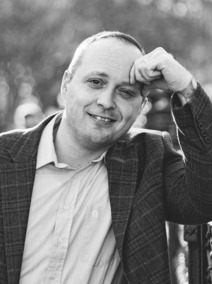 Black-and-white photo of a person smiling, wearing a plaid blazer and a light shirt.