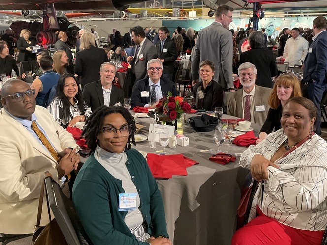 Nine people seated at a table in a busy banquet setting.