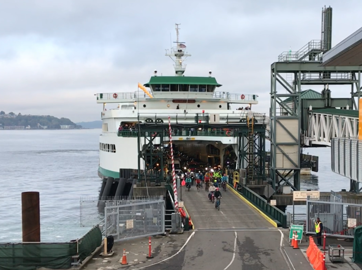 Ferry docked at Seattle terminal with passengers bicyclists disembarking the vessel on a vehicle transfer span.