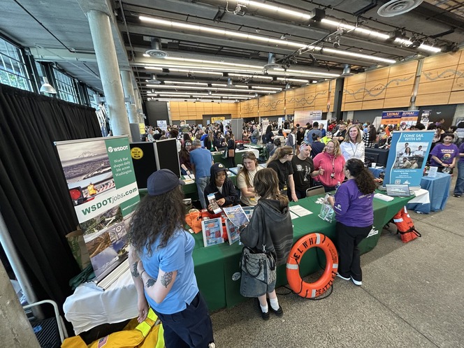 Career fair with multiple booths and attendees in a large indoor venue. Prominent "WSDOT" signage is visible.