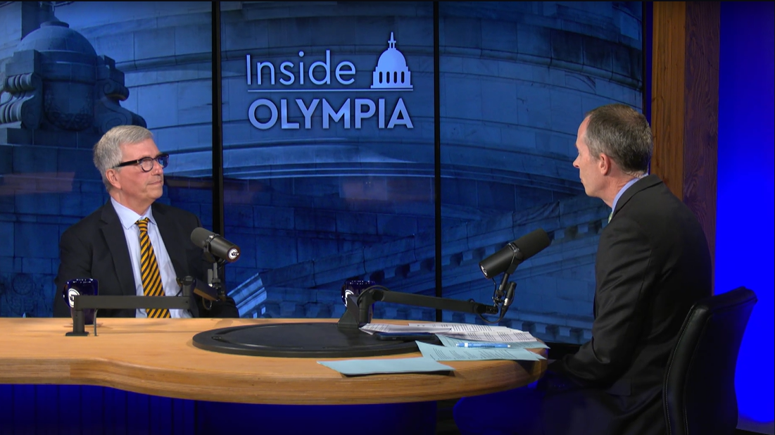 Two people seated at a table with microphones, in a studio setting with "Inside Olympia" on the backdrop.