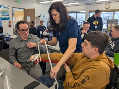 A woman instructs two people seated how to use a splint.