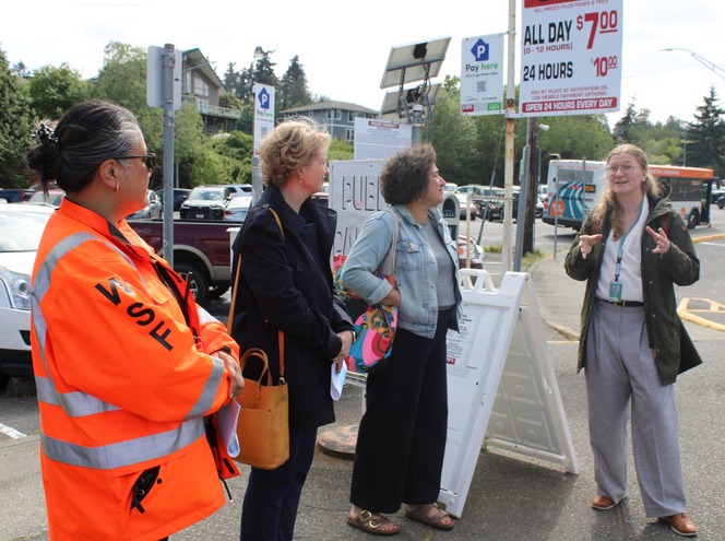 Four people standing in near the parking area at Southworth terminal with signs and vehicles in the background.