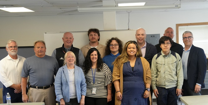 A group of 12 people pose for a photo together in a classroom setting.