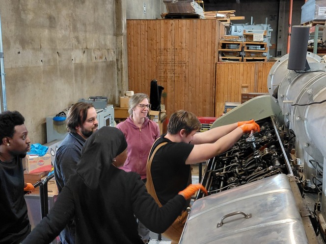Group of people working on a large industrial machine in a workshop.
