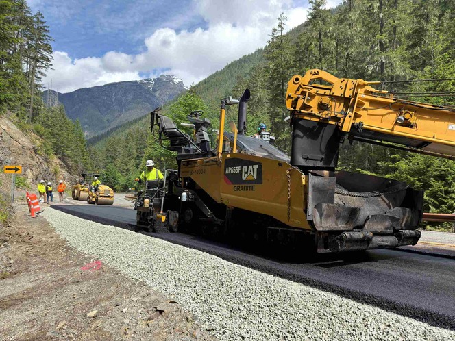 A large yellow paver places asphalt along a mountainous section of SR 20/North Cascades Highway.