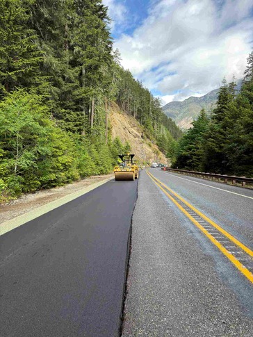 A roller compacts fresh asphalt along a mountainous section of SR 20/North Cascades Highway.