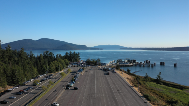 Aerial view of Anacortes terminal with a large, empty parking lot, a dock, water and hills in the background.