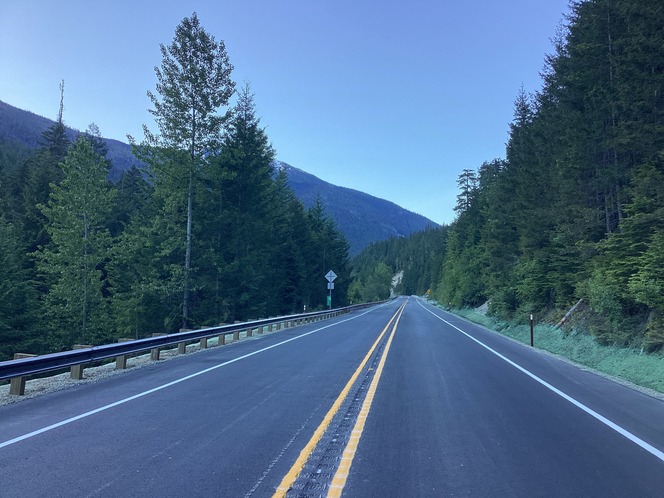 Fresh asphalt and lane markings along a repaired section of SR 20/North Cascades Highway in the mountains on  sunny morning.