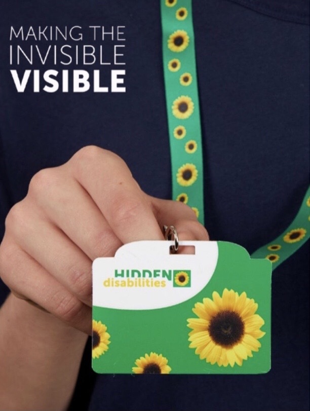 Person holding green ID card for "Hidden Disabilities," featuring sunflowers, with a lanyard around their neck.