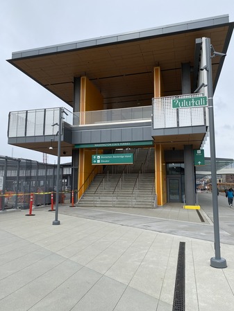 Exterior view of Seattle terminal featuring a two-story structure and a green sign that says "ʔulułali" in the foreground.