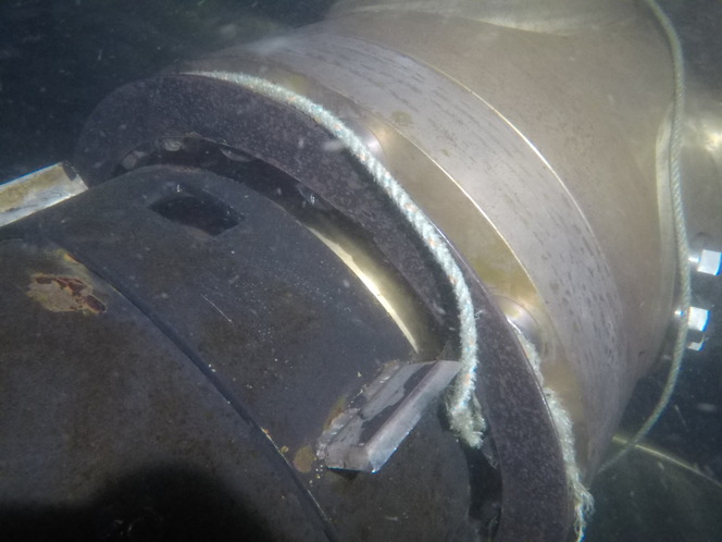 Close-up of ferry's rudder underwater, showing a rope coiled around metal parts with bolts.