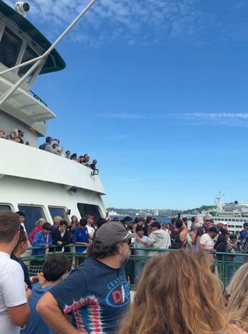Outdoor ferry decks full of people enjoying a sunny day. Blue sky and another ferry in the background.