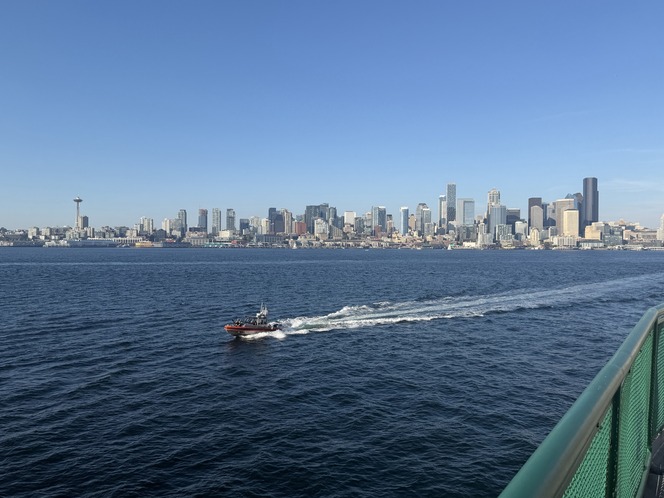 Panoramic view of Seattle's skyline seen from a ferry with a small orange Coast Guard boat in the foreground.