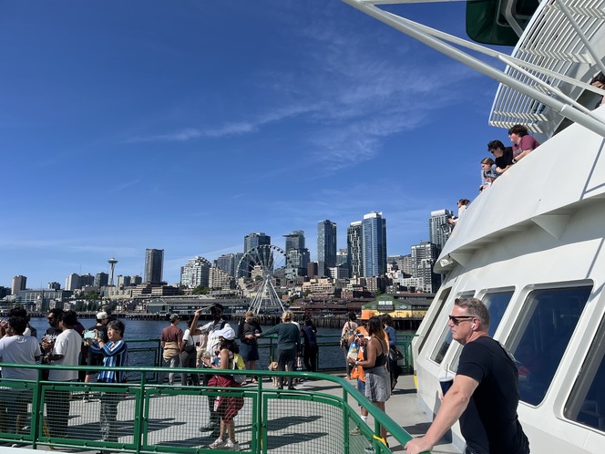 View from a ferry showing passengers enjoying the Seattle skyline under a clear blue sky.