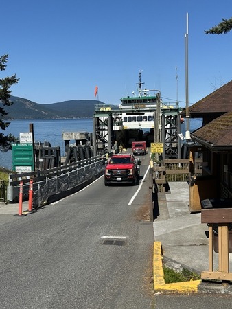 Two red fire department vehicles approach departing a ferry at a dock on a sunny day.