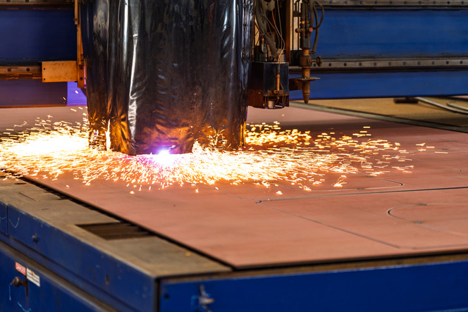 A plasma cutting machine emits sparks while cutting through material on a metallic work surface, surrounded by blue machinery.