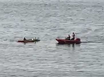 Two boats on calm water: a kayak with one person and a larger red rescue boat with two people.