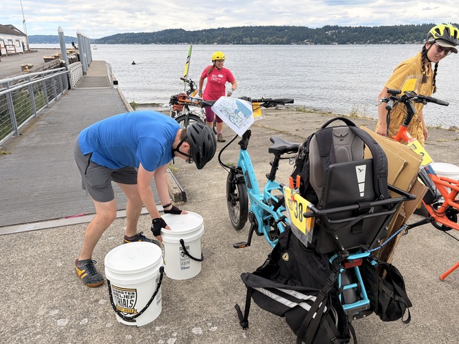 people wearing helmets prepare buckets of water to be strapped to cargo bikes