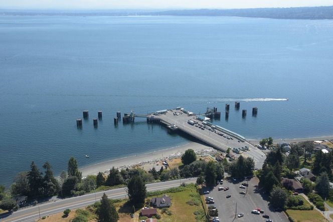 Aerial view of a Clinton terminal with parked cars visible on the nearby road and the Snohomish County shoreline in the far background.