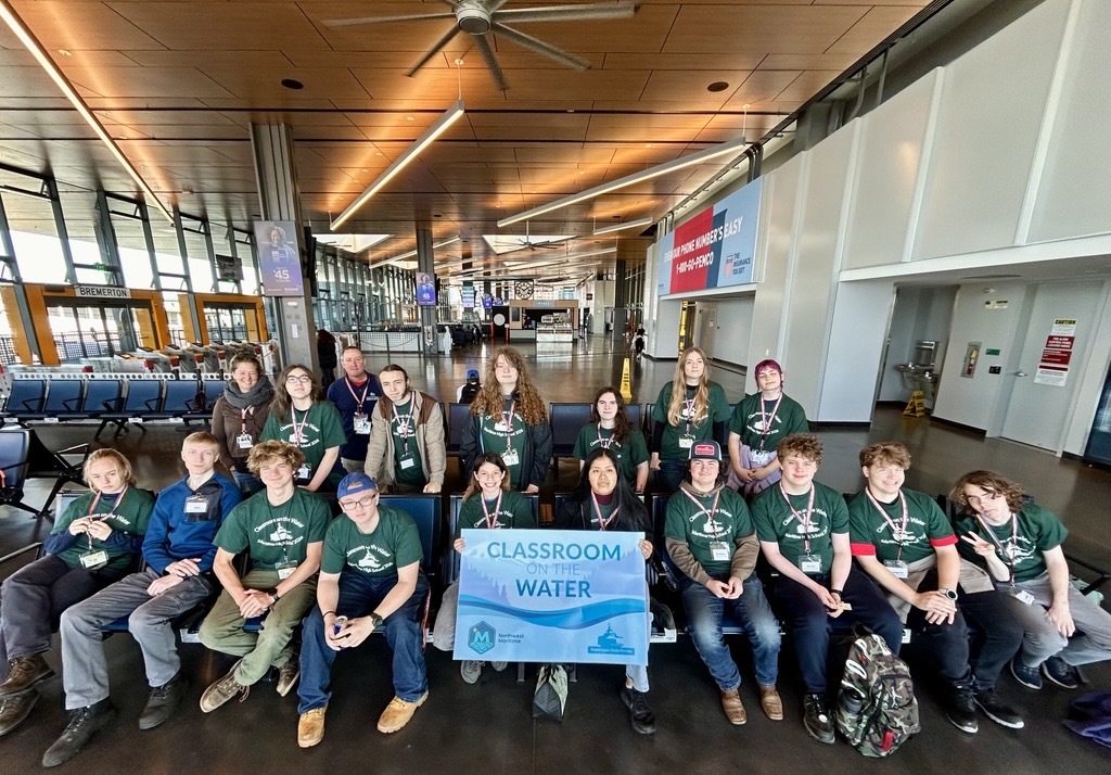 Group posing in the Seattle terminal building while holding a “CLASSROOM ON THE WATER” sign.