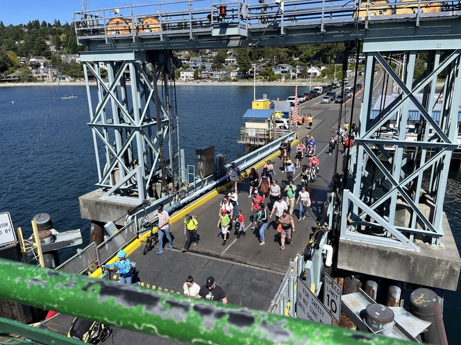 People walk and roll on a vehicle transfer span onto a ferry's car deck at Fauntleroy terminal.