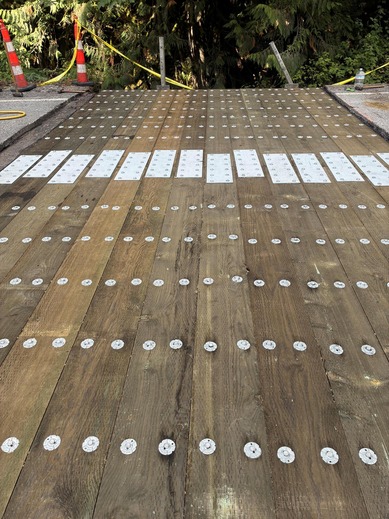 A new timber decking for the SR 9 Lake Creek Bridge is shown, with orange construction candlesticks in the background.