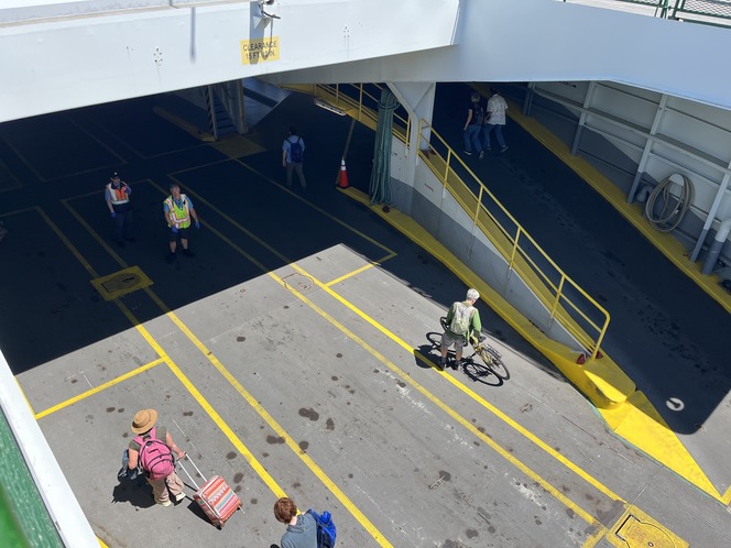 Overhead view of passengers, workers, a bicycle, and luggage onto a ferry's car deck.