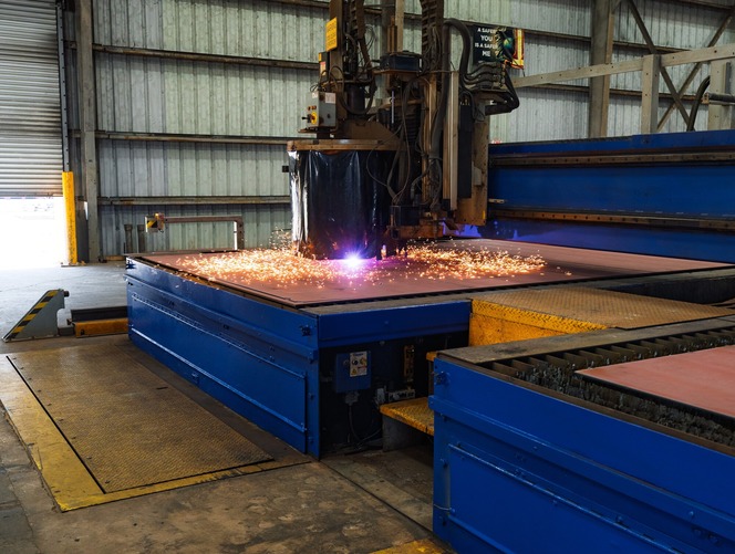 Industrial plasma cutter cutting a metal sheet, producing a bright arc and a spray of orange sparks.