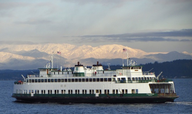 White-and-green passenger ferry named Tilikum crossing blue water with sunlit mountains in the background.