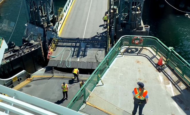 Workers in safety vests work aboard a ferry, untying the vessel from the dock to prepare for its sailing.