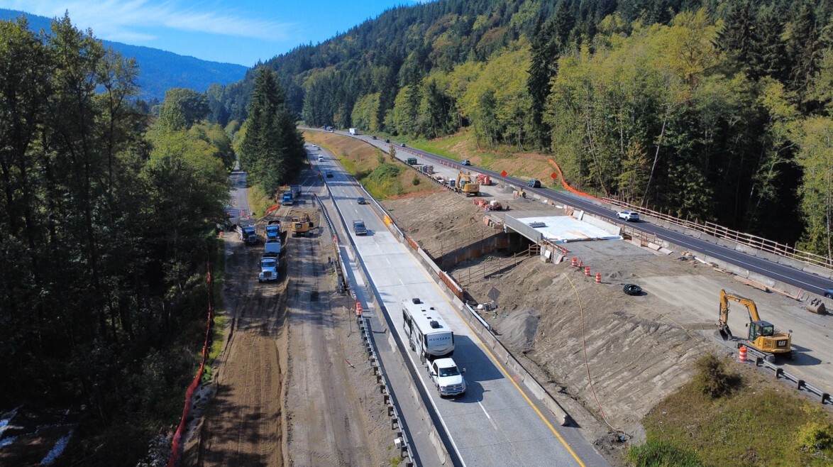 Aerial photograph of northbound and southbound I-5 shows highway construction through a forested mountain valley.