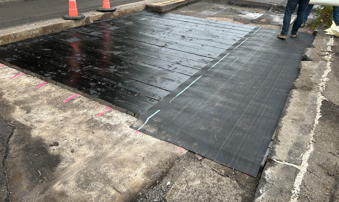 A black waterproof covering on a section of State Route 9 where the asphalt has been removed.