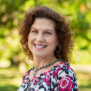 Portrait photo of Heather Bartlett. Her hair is red, eyes are green, she is white. Her blouse is hot-pink, swirly flowers.