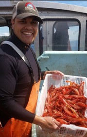 Tyson on a boat holding a bucket of harvested shrimp.