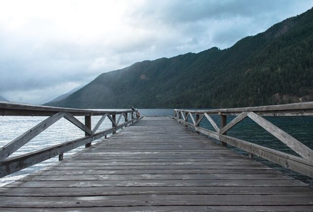 Wooden dock over dark blue water ringed with forested mountains. 