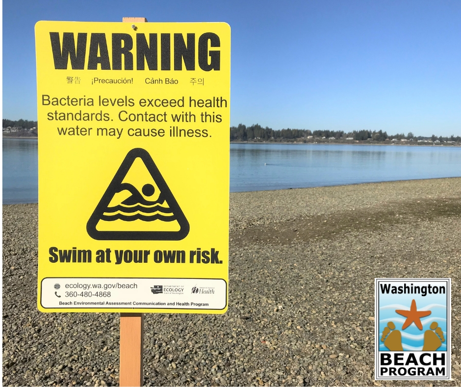 Yellow sign on a beach warning of an advisory at the beach due to high bacterial levels.