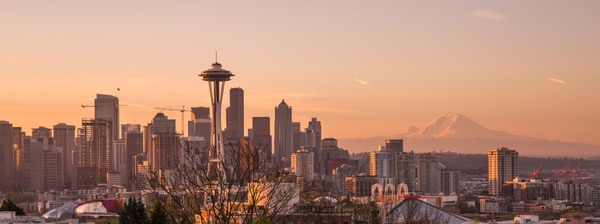 The downtown Seattle skyline stands in front of Mount Rainier as sunset turns the sky orange. 