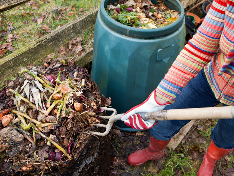 A person uses a pitchfork to turn their pile of compost