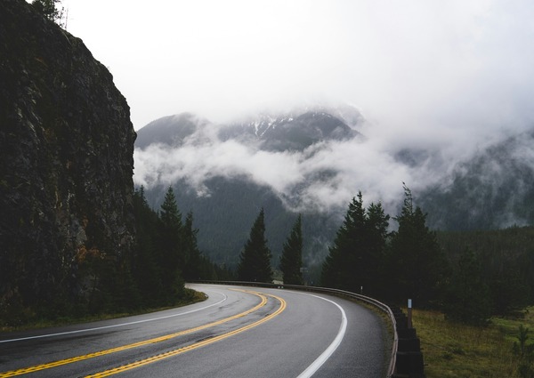 Grey road between a green grass field and mountain during daytime