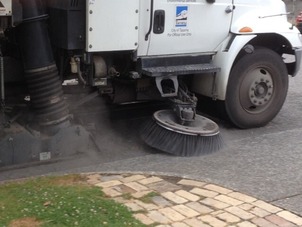 Road and sidewalk with grass and pavers - street sweeper cleaning road.