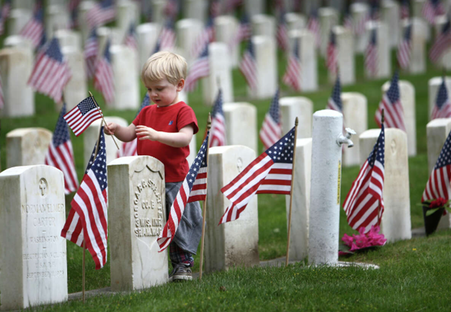 Military Appreciation Month May 2024 - Little boy placing flags at a Veterans cemetery.