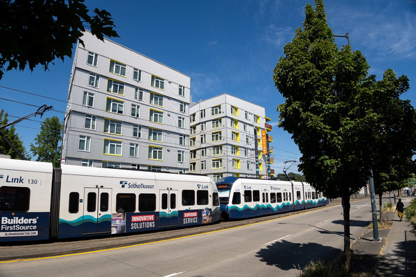 A train passes an affordable housing development on a tree-lined urban street.