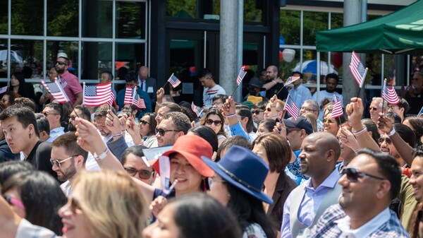 Large group of people standing outdoors, several waving small American flags