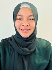 Kalimah, a Black and Indigenous Muslim American woman, wears a green hijab facing the camera and smiling. Her shirt is a similar green to her hijab. 