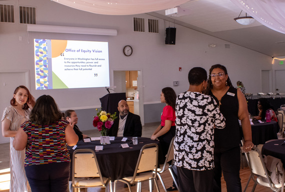 A group of diverse people,  both sitting and standing, are interacting and talking with each other at an event. 